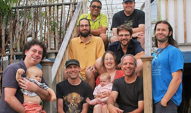 Portrait de groupe représentant neuf adultes et deux bébés, assis sur un porche en bois.